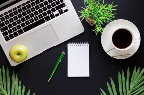 A dark desk flatlay with a notebook and pen